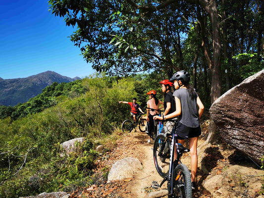 Group of people with bicycles on a mountain trail with trees and mountains in the background.