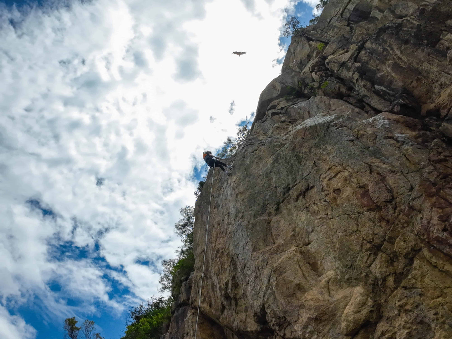 Person abseiling down a rocky cliff with a blue sky and clouds in the background