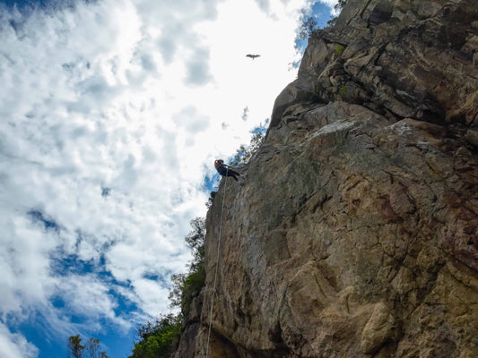 Person abseiling down a rocky cliff with a blue sky and clouds in the background