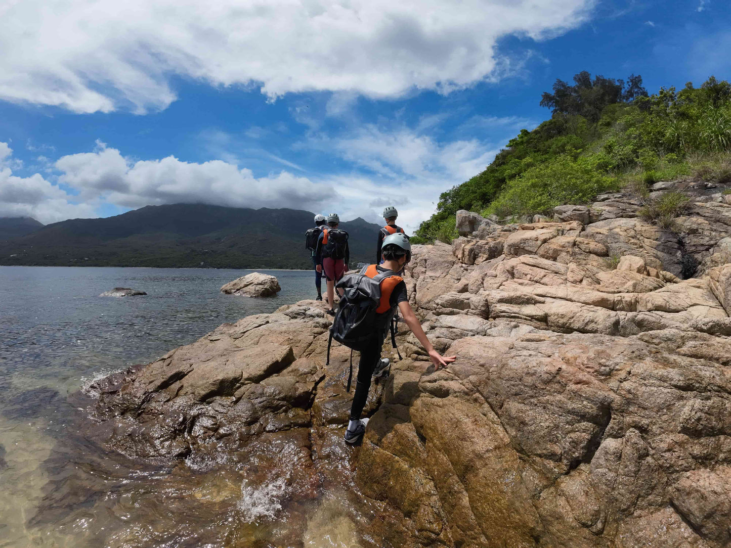 Kids on a rocky shoreline with mountains and trees in the background