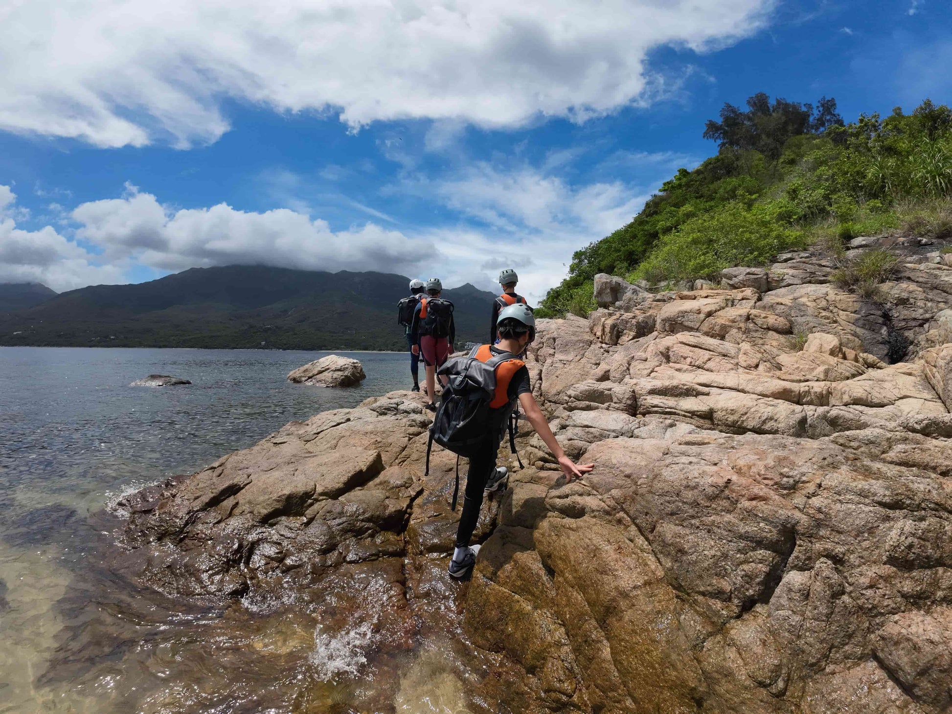 Kids on a rocky shoreline with mountains and trees in the background