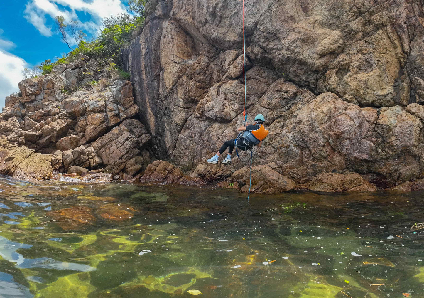 Person rappelling down a rocky cliff into clear water