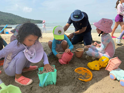 Children playing in the sand on a beach with toys and adults supervising.