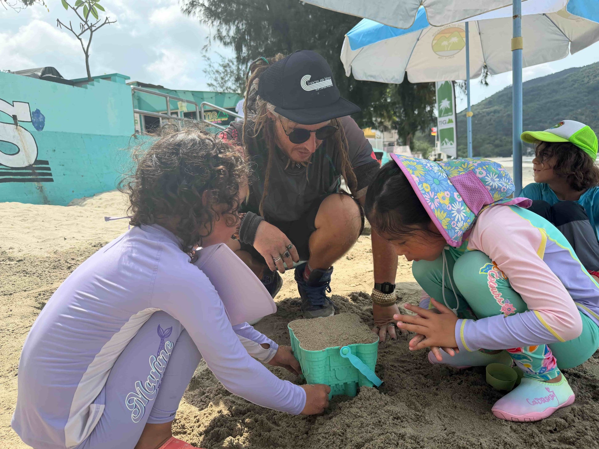 Group of people, including children, playing with sand on a beach.