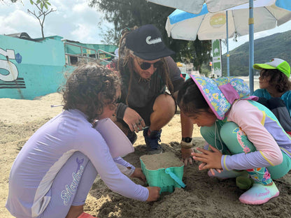 Group of people, including children, playing with sand on a beach.
