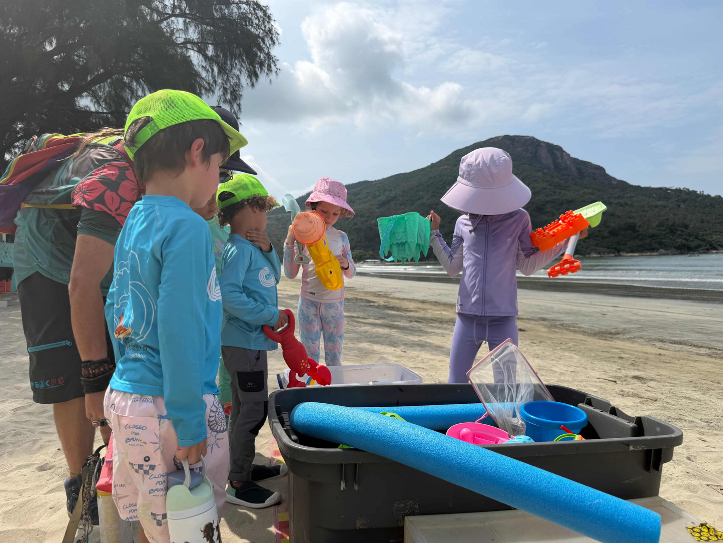 Children playing with beach toys on a sandy beach with mountains in the background