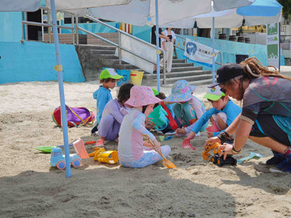 Children playing in the sand with toys under umbrellas on a beach.