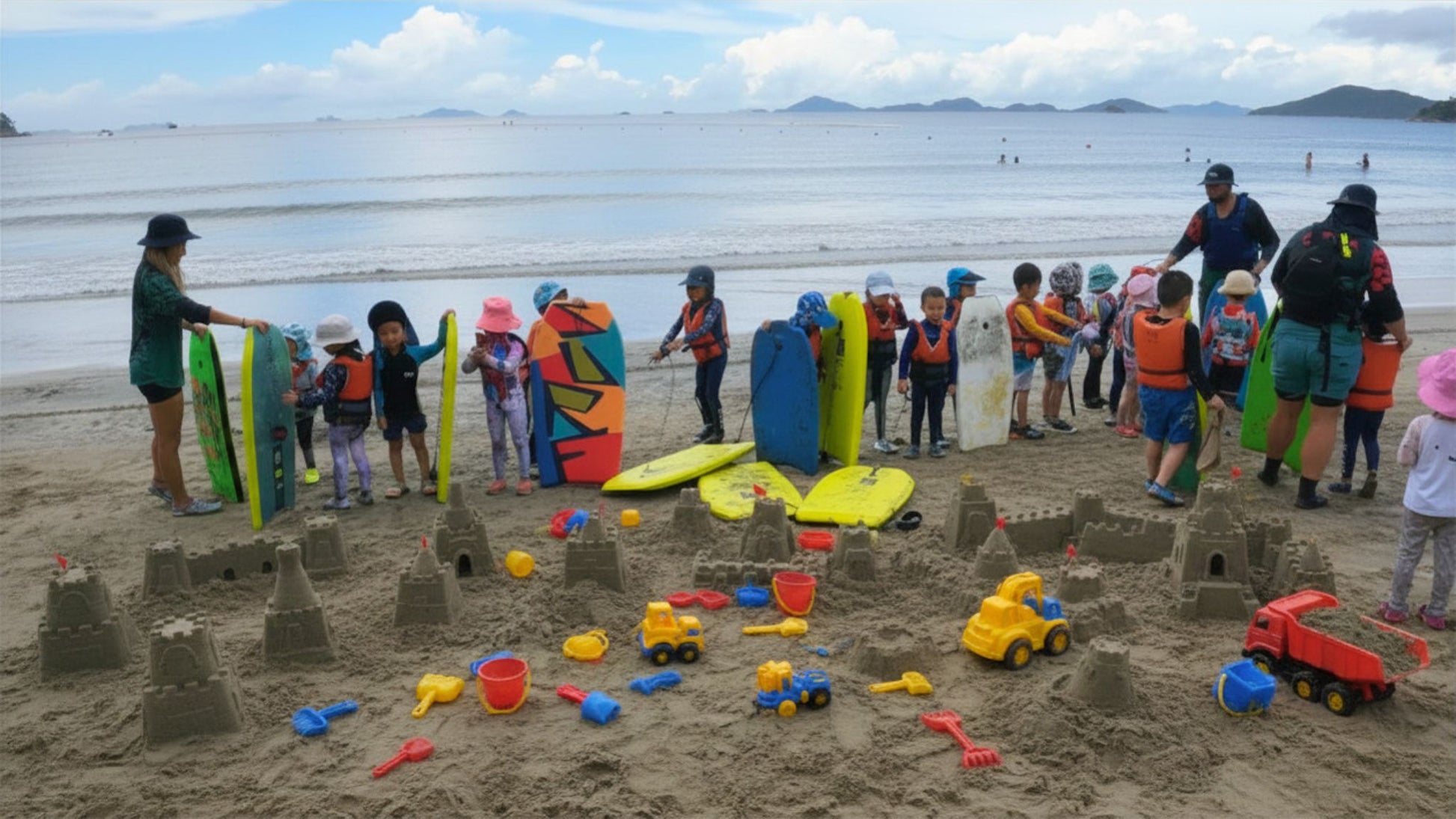children on beach with sandcastles and body boards